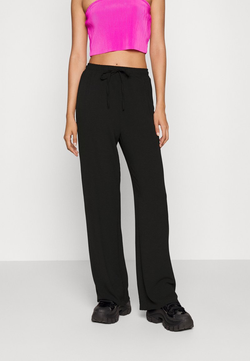 Pantaloni neri a gamba larga realizzati in un tessuto morbido con vita regolabile, abbinati a un top corto a coste rosa brillante e sneakers nere chunky.