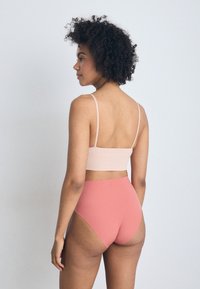 Csíkozott, világos rózsaszín crop top vékony pántokkal, amelyet magas derekú, sima korall alsótesttel párosítanak. Mindkét ruha minimalista dizájnt mutat.