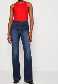 Rode geribbelde tanktop gecombineerd met high-waisted wijde blauwe spijkerbroek. De denim heeft zakken en lichte vervaging. Zwarte enkelboots maken de look compleet.