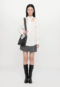 White button-up shirt with cut-out detail, gray pinstriped skirt with text, black shoulder bag, knee-high black boots, smooth texture.