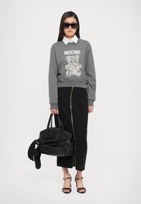 Felpa grigia con grafica di un orso, gonna nera con zip dorata, borsa nera, occhiali da sole neri e sandali neri con cinturini.