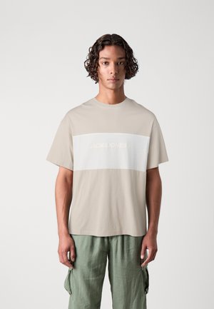 Lys beige t-shirt med en vandret hvid panel, der har prægede "JACK&JONES" tekst. Korte ærmer og et rundhals design.