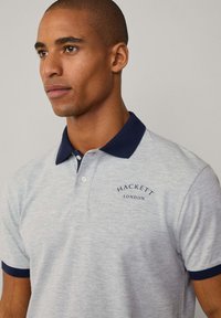 Šedé polo tričko s námořnickými akcenty na límci a rukávech, se malým logem "Hackett London" na hrudi. Materiál bavlna, klasický střih.