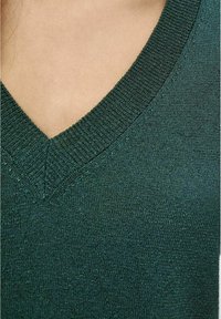 Suéter de cuello en V en verde oscuro, con un patrón de punto texturizado y un dobladillo acanalado. La tela tiene un brillo sutil y un acabado suave.