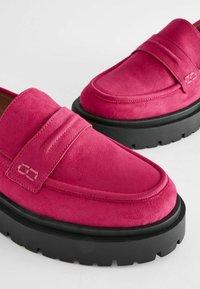 Loafers din suede roz strălucitor, cu o cusătură proeminentă, având o talpă groasă din cauciuc negru, cu caneluri adânci pentru aderență.