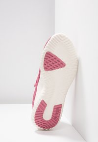 Rosa idrottssko med sula i strukturerat vitt mellansole, som har ett mönstrat gummigrepp och en präglad logotyp. Böjd form och robust design.