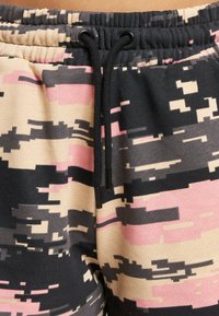 Cotton jogger pants featuring a digital camouflage pattern in pink, black, and beige, with an adjustable black drawstring at the waist.