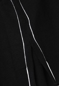 Schwarzes Strickkleidungsstück mit weißen Akzentstreifen an den Seiten. Verfügt über einen strukturierten Stoff und ein dezentes Schlitzdetail nahe dem Saum.