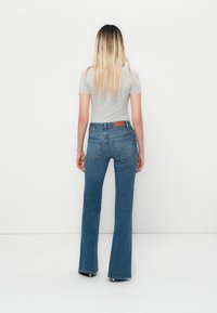 Blå utsvingte jeans med høy midje, med en lærtags og baklommer, kombinert med en tettsittende grå t-skjorte med korte ermer.