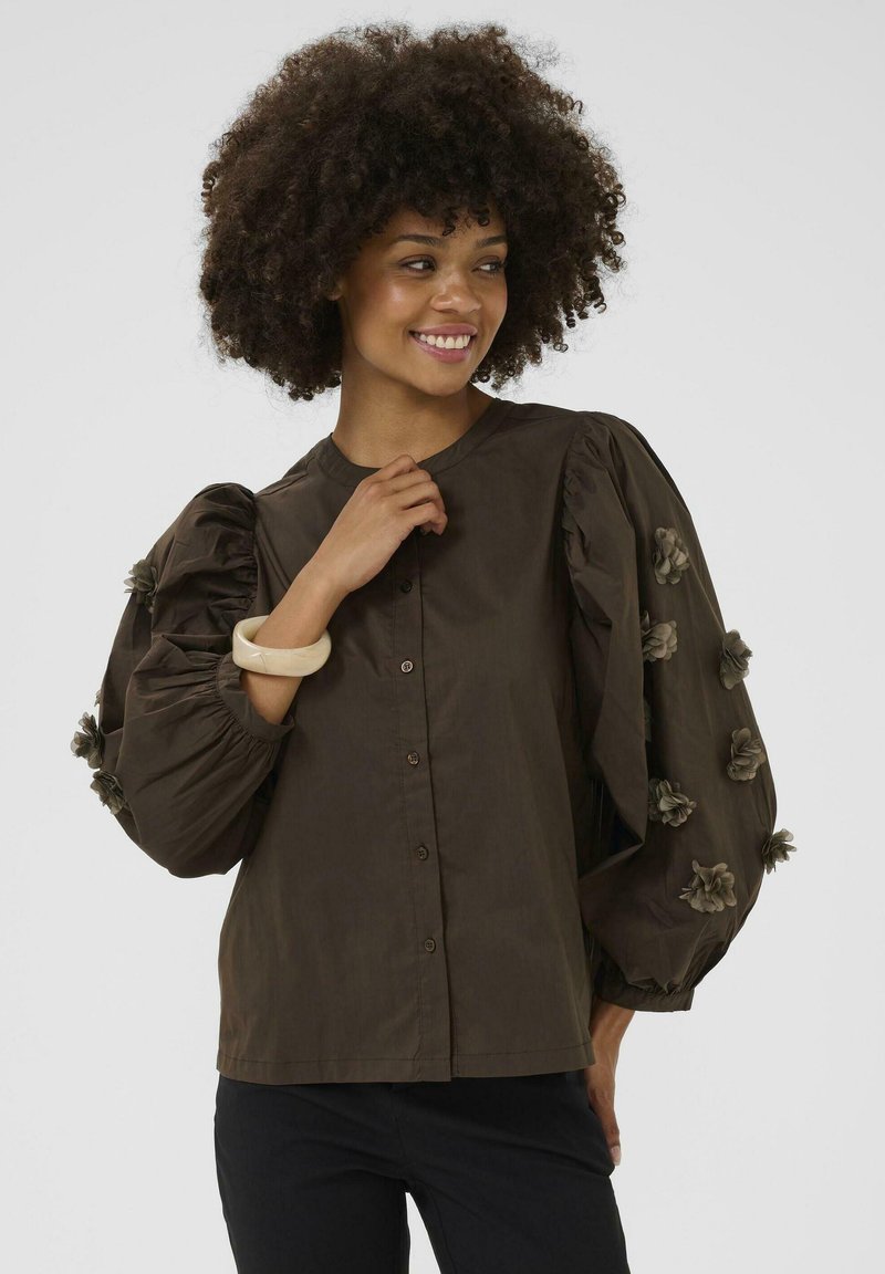 Brown blouse with large, puffed sleeves and floral embellishments. It features a button-down front and a round neckline.