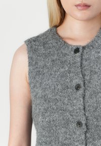 Maglione grigio lavorato a maglia senza maniche con colletto rotondo e cinque bottoni neri, realizzato in un morbido tessuto di lana testurizzata.