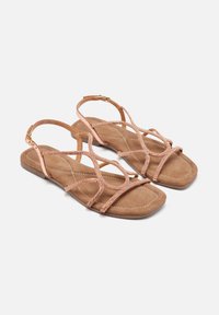 Sandalias de oro rosa con suela plana, plantilla de ante y correas cruzadas decoradas con pequeños cristales. Tira ajustable en el tobillo con herrajes dorados.