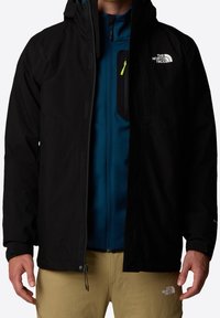 Schwarze wasserdichte Jacke mit Kapuze, ausgestattet mit Reißverschlüssen, verstellbaren Bündchen und einem Logo auf der Brust. Eine blaue Innenschicht ist sichtbar.