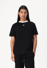 Svart t-shirt med rund hals och korta ärmar, med en vit logotyp på bröstet, tillverkad av ett mjukt tyg, i kombination med svarta joggingbyxor.