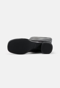 Bottine en cuir noir avec un bout arrondi et un petit talon bloc. La semelle est en caoutchouc texturé, offrant une bonne adhérence. Surface supérieure lisse.