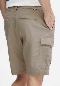 Beige cargo shorts laget av et lett stoff, med to baklommer og en sidelomme, samt en subtil logo detalj på midjebåndet.