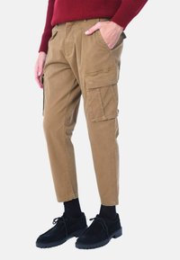 Pantaloni cargo color khaki con più tasche laterali, una vestibilità comoda e un tessuto liscio e resistente. Abbinati a scarpe nere e calzini.