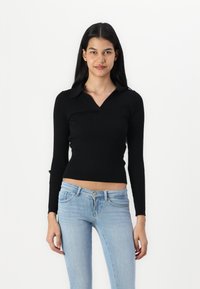 Black ribbed long-sleeve top with a collared neckline, fitted design, and smooth texture, paired with light blue slim-fit jeans.