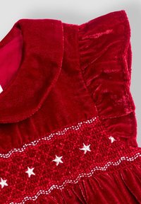 Rotes Samtkleid mit einem Peter-Pan-Kragen, das ein gerüschtes Element mit weißen Sternmustern aufweist. Rüschensleeves und glatte Textur.