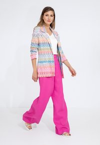 Blazer tessuto multicolore con motivo a zigzag, abbinato a pantaloni di lino rosa a vestibilità ampia e sandali bianchi con cinturini.
