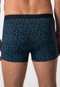 Kraťasy na boxerky s tmavě modrým pozadím, zdobené vzorem malých modrých listů. Elastický pas se zvlněným logem.