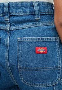 Μπλε τζιν σορτς με κόκκινο και κίτρινο λογότυπο "Dickies" στο πίσω τσέπη. Καθαροί γραμμές με ορατή ραφή και κλασική ζώνη μέσης.