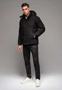 Svart vadderad jacka med huva, med ett rutigt mönster, guldknappar och sidofickor. Bärs med svarta byxor och vita sneakers.