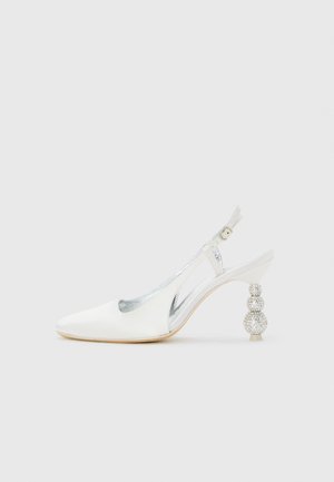 Zapato de tacón alto en piel blanca con diseño slingback, puntera afilada y tacón redondo decorado con strass, sobre un fondo sencillo.