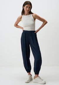 Marineblaue, leichte Jogginghosen mit elastischem Bund und Bündchen. Kombiniert mit einem eng anliegenden weißen Tanktop und weißen Turnschuhen.