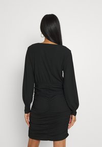 Robe noire à manches longues, texture côtelée et détails froncés à la taille et à la jupe. Se termine au-dessus du genou. Design simple et élégant.