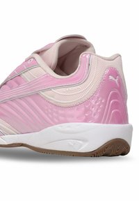 Rozā sporta apavi ar teksturētu sintētisku uzdari, baltiem akcentiem un izliekto, mīksto zoli. Ietver režģa paneļus un zīmola detaļas.