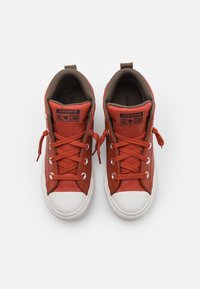 Czerwone skórzane buty Converse All Star w wersji wysokiej, z białymi gumowymi czubkami, brązowym wnętrzem i płaskimi sznurowadłami, z akcentami logo.