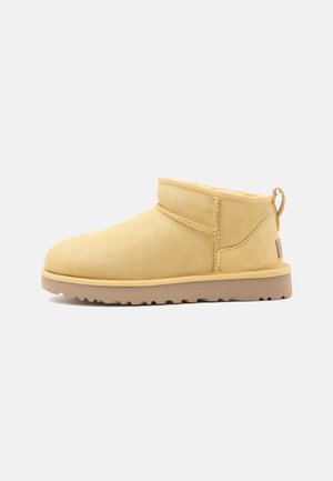 Kurzer beiger Wildleder-Stiefelette mit flacher Gummisohle, sichtbarer Naht und Lasche hinten vor schlichtem Hintergrund.