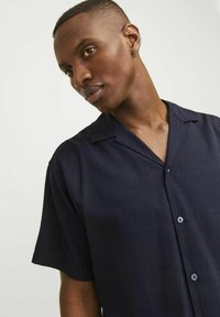 Short-sleeve button-up shirt in navy blue, featuring a relaxed collar and smooth texture with subtle textured pattern. Buttons are in contrasting color.