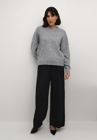 Grå strikket sweater med rund hals, parret med vide sorte bukser og spidse sorte sko. Blød tekstur og afslappet pasform.