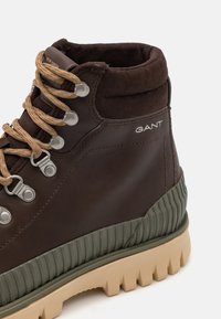 Brązowe skórzane buty trekkingowe z beżowymi sznurówkami, srebrnymi oczkami, wyściełanym kostką i teksturowaną zielono-beżową gumową podeszwą. Logo GANT po boku.