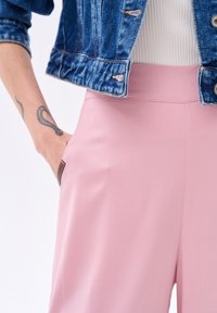 Różowe spodnie z wysokim stanem o gładkiej fakturze i bocznymi kieszeniami, w połączeniu z dżinsową kurtką i białym, prążkowanym topem.