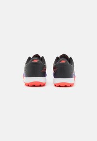 Baskets de sport noires au design épuré, avec des accents rouges et violets, une surface texturée et une semelle blanche avec un motif de traction.