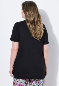 Svart kortärmad t-shirt, avslappnad passform, i kombination med flerfärgad mönstrad leggings. Slät textur, enkelt mönster, medellång täckning.