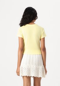 Camiseta amarilla corta de manga corta, combinada con una falda blanca de encaje con dobladillo festoneado y un patrón de calados.
