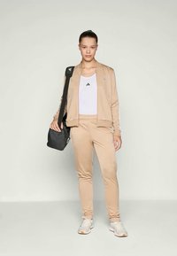 Bežna športna obleka, sestavljena iz zip-up jakne in prilegajočih hlač, v kombinaciji z belo majico na naramnice in črno torbo čez ramo. Look dopolnjujejo teniske.