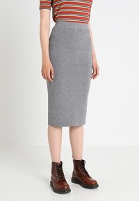 Šedá vlněná tužková sukně s vysokým pasem a přiléhavým střihem, oblečená s hnědými šněrovacími kotníkovými botami a pruhovaným tričkem.