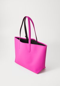 Roze tote bag van glad synthetisch materiaal, met twee zwarte stoffen handvatten en een open ontwerp. Binnenkant is zwart zonder zichtbare sluitingen.