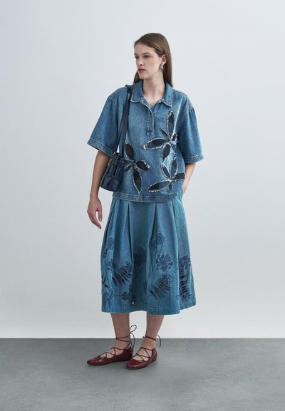 Chemise en denim avec broderies florales, associée à une jupe plissée en denim aux motifs similaires. Ballerines marron à lacets. Sac à main minimaliste.