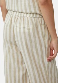 Pantalons en lin rayés beiges légers avec une taille élastique, dotés de poches latérales et d'une coupe décontractée, mis en valeur par des rayures verticales.