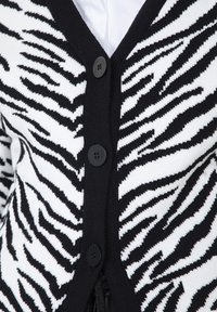 Cardigan a strisce zebrate in bianco e nero con scollo a V, caratterizzato da quattro bottoni neri e un tessuto a maglia testurizzato.