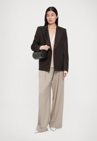 Blazer marrón de doble botonadura sobre una blusa beige, combinado con pantalones ancho beige y zapatos de punta crema. Llevando un bolso cilíndrico negro.