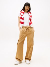 Bílý tričko, pískové cargo kalhoty s bočními kapsami, červený a bílý pruhovaný svetr přehozený přes ramena, bílé tenisky. Neformální oblečení.