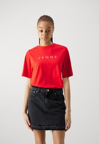 T-shirt en coton rouge avec le texte "FEMME" en blanc, associé à une mini-jupe en denim noir avec un ourlet effiloché et des poches avant.
