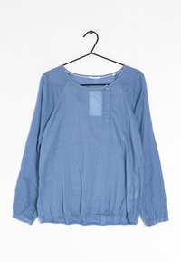 Camicia a maniche lunghe azzurro chiaro in tessuto con pois bianchi, con scollatura tonda e orlo elasticizzato. Dettaglio di piccolo bottone sul davanti.
